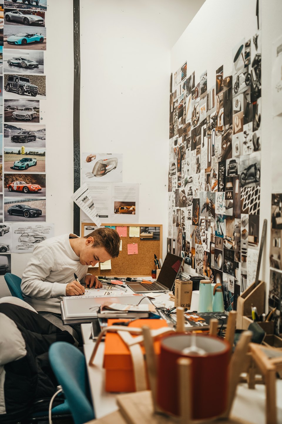 Un product designer disegna modelli di auto su una scrivania affollata in uno studio.