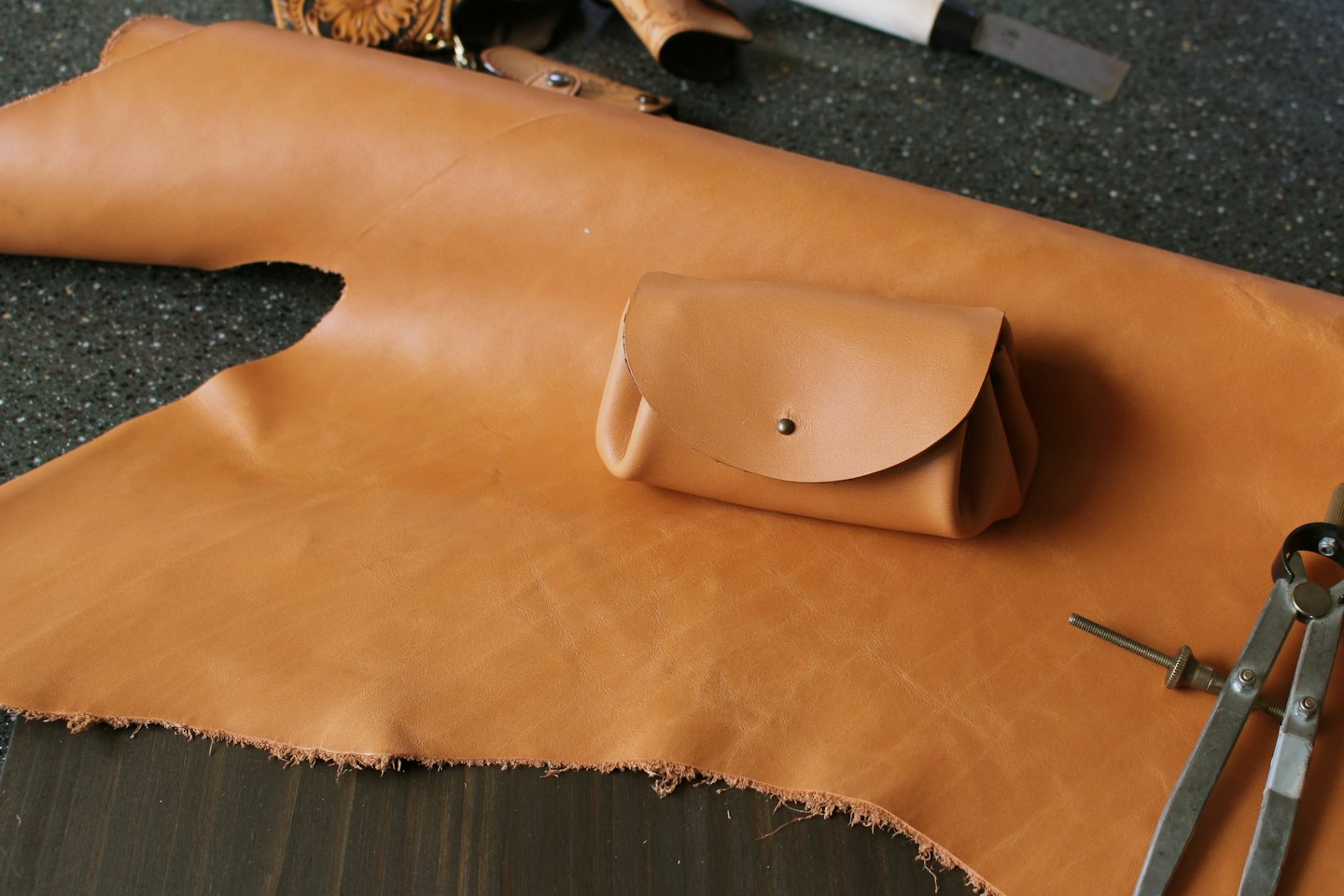 Sacchetto di pelle con borchia in ottone appoggiato su un foglio di pelle.